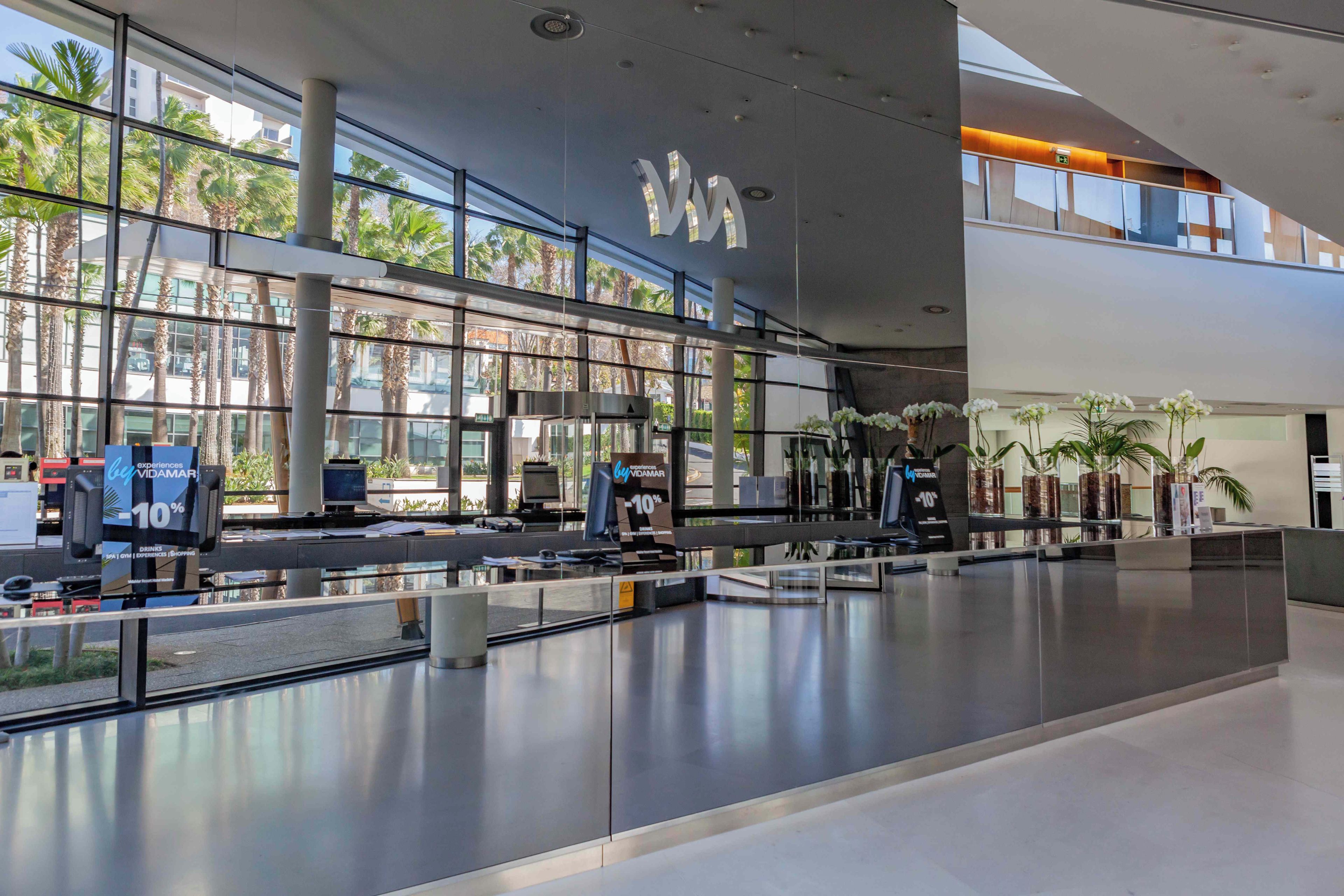 A spacious airport terminal with a modern design, featuring a check-in area with self-service kiosks and a clear view of palm trees outside.