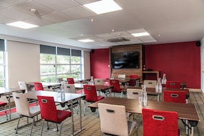 A conference room with multiple tables and chairs, large windows, and a television screen. - Holiday Inn Express Glasgow Airport by IHG (Paisley)
