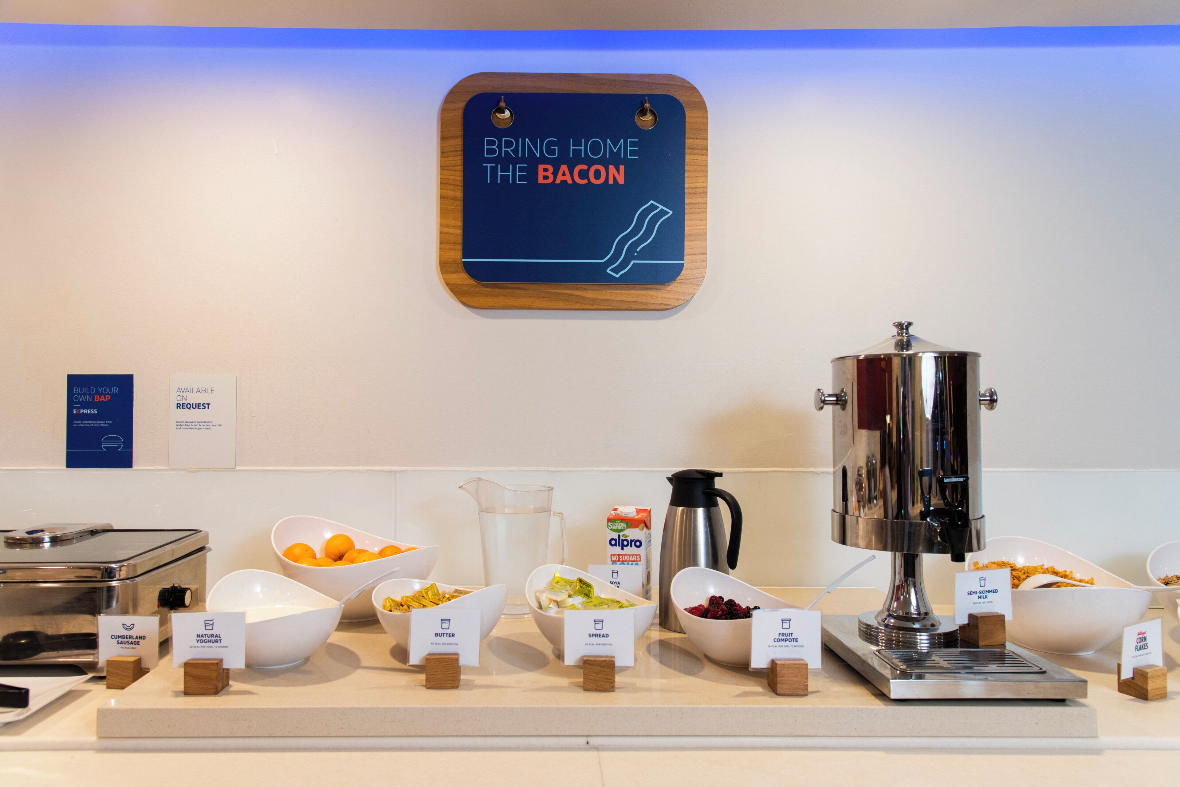 Un bufé de desayuno con diversas opciones de comida y un cartel que indica la disponibilidad de tocino.