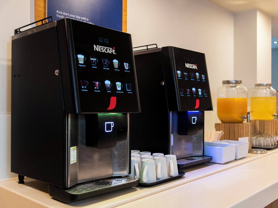Duas máquinas de café Nescafé com seleção de opções de café e um dispensador de água.