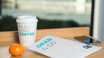 A coffee cup with text, a piece of paper with 'GRAB & GO' written on it, an orange, and a smartphone on a wooden surface.