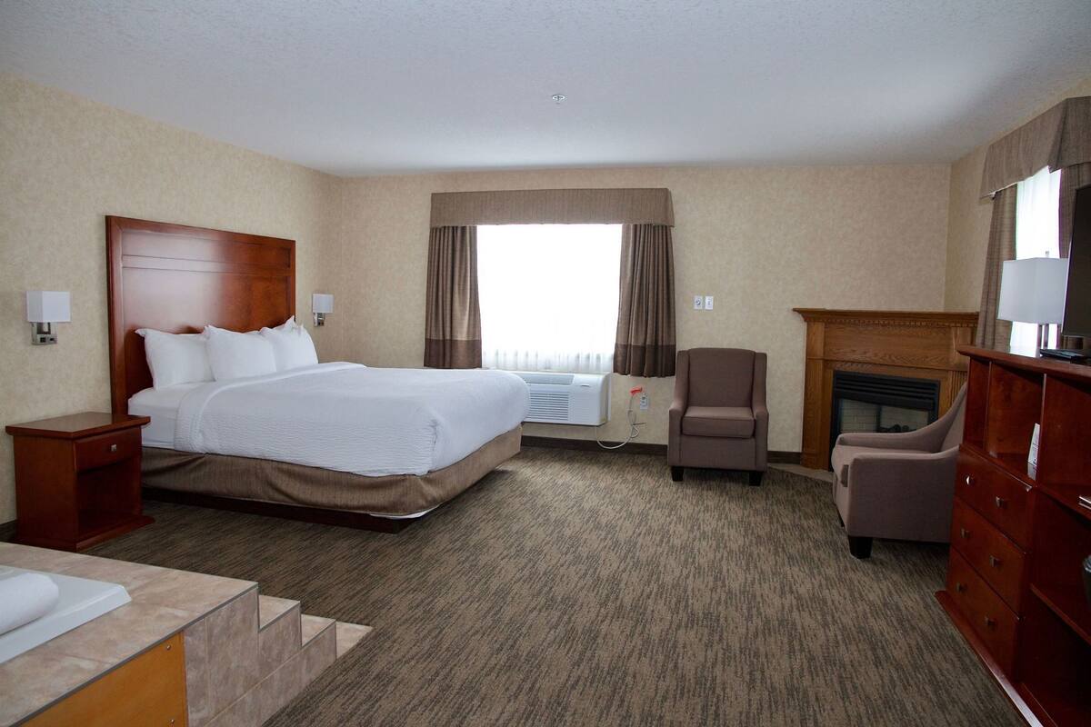 A hotel room with a bed, a chair, a dresser, a TV, and a fireplace.