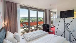 Une chambre d’hôtel avec un lit, une télévision, un balcon avec des chaises et une vue sur la ville.