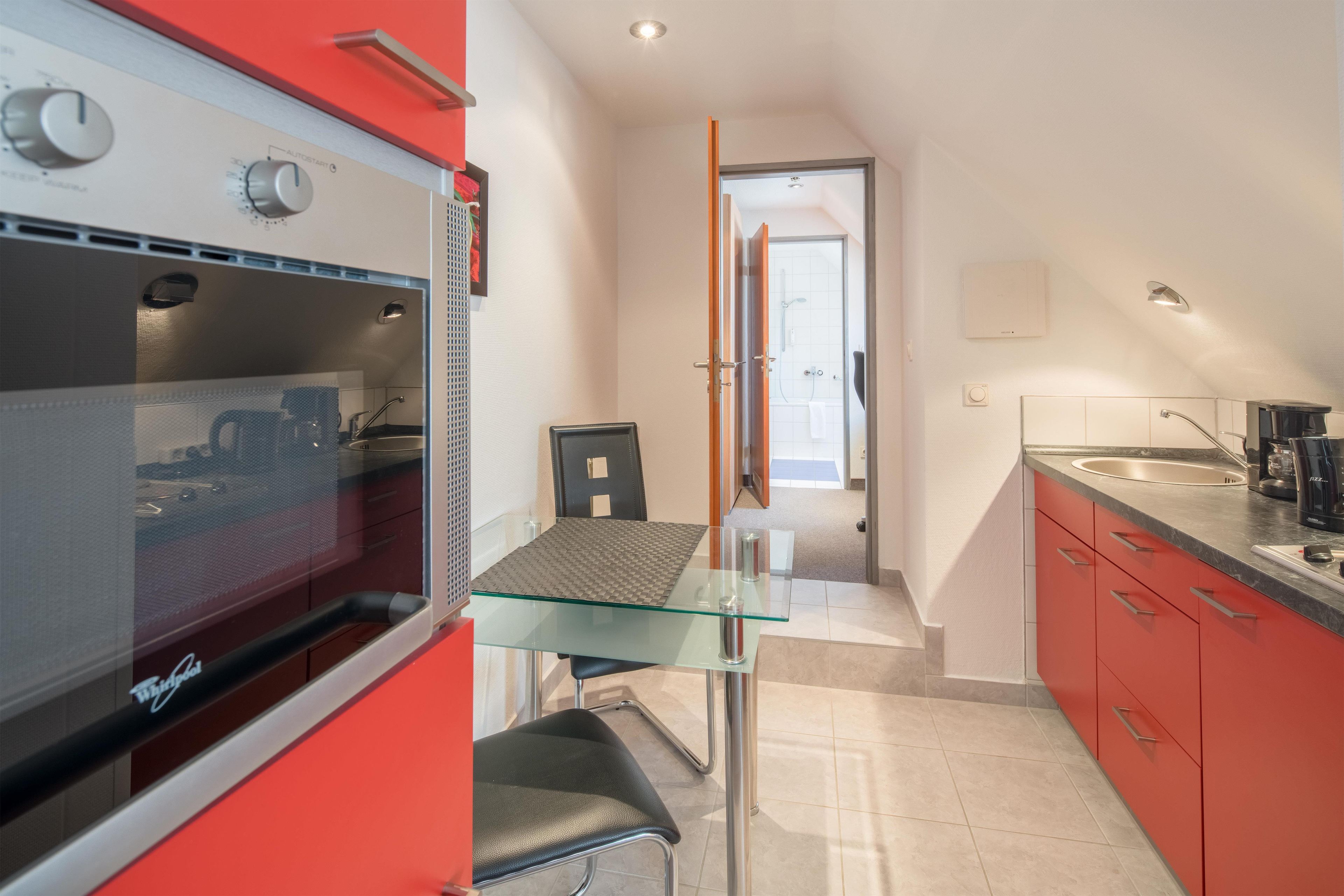 A compact kitchen with a glass-top table, a built-in oven, and red cabinetry.