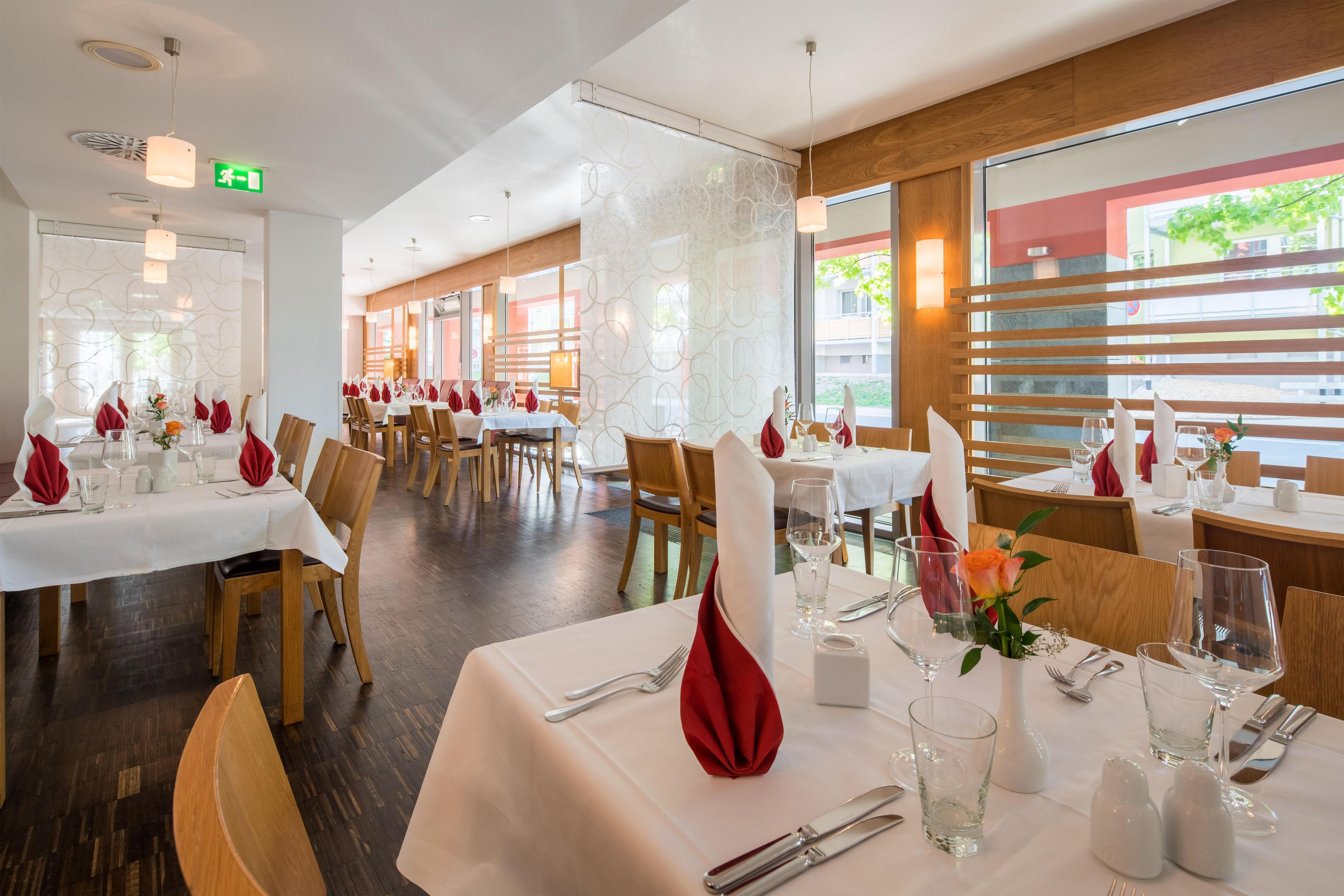 A restaurant with multiple tables set for dining, featuring white tablecloths and red napkins.