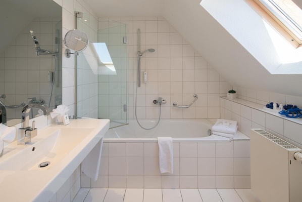 Un baño moderno con ducha de mampara de vidrio, bañera independiente y tocador con espejo.