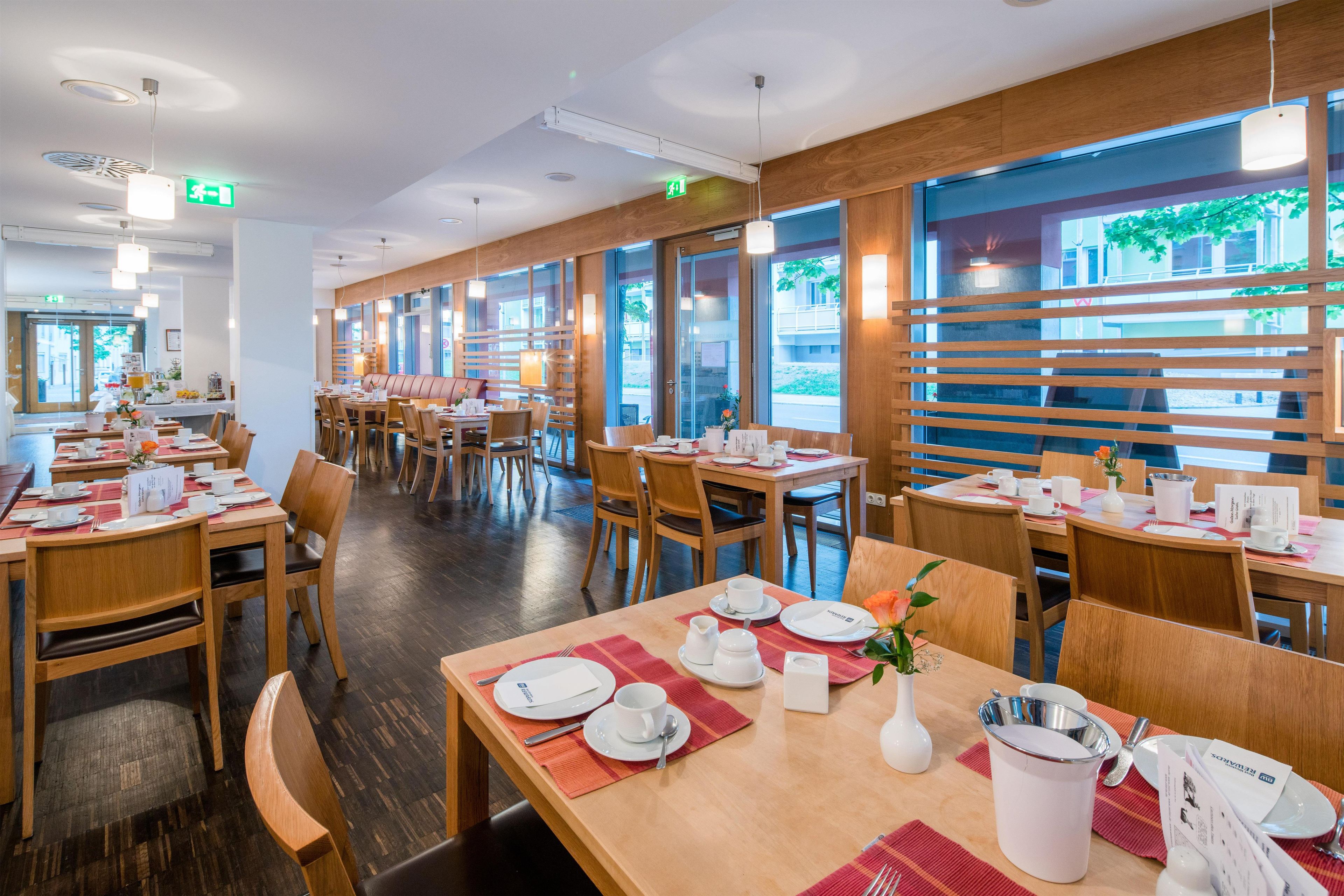 A restaurant with multiple tables, wooden flooring, and large windows allowing natural light.