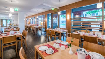 A restaurant with multiple tables, wooden flooring, and large windows allowing natural light.