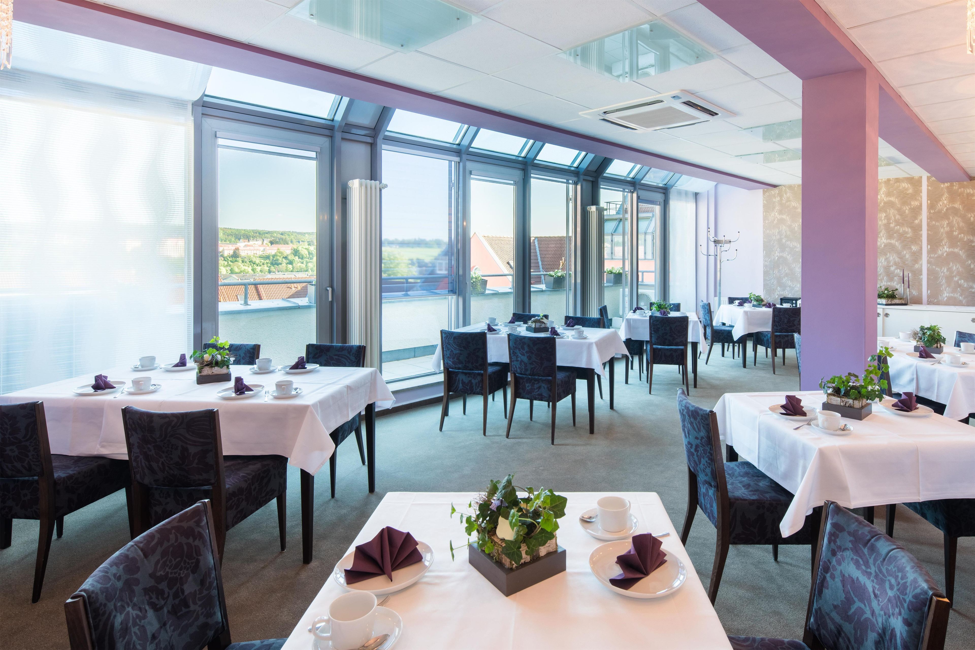 Un restaurante con varias mesas y sillas, amplios ventanales y vistas al exterior.