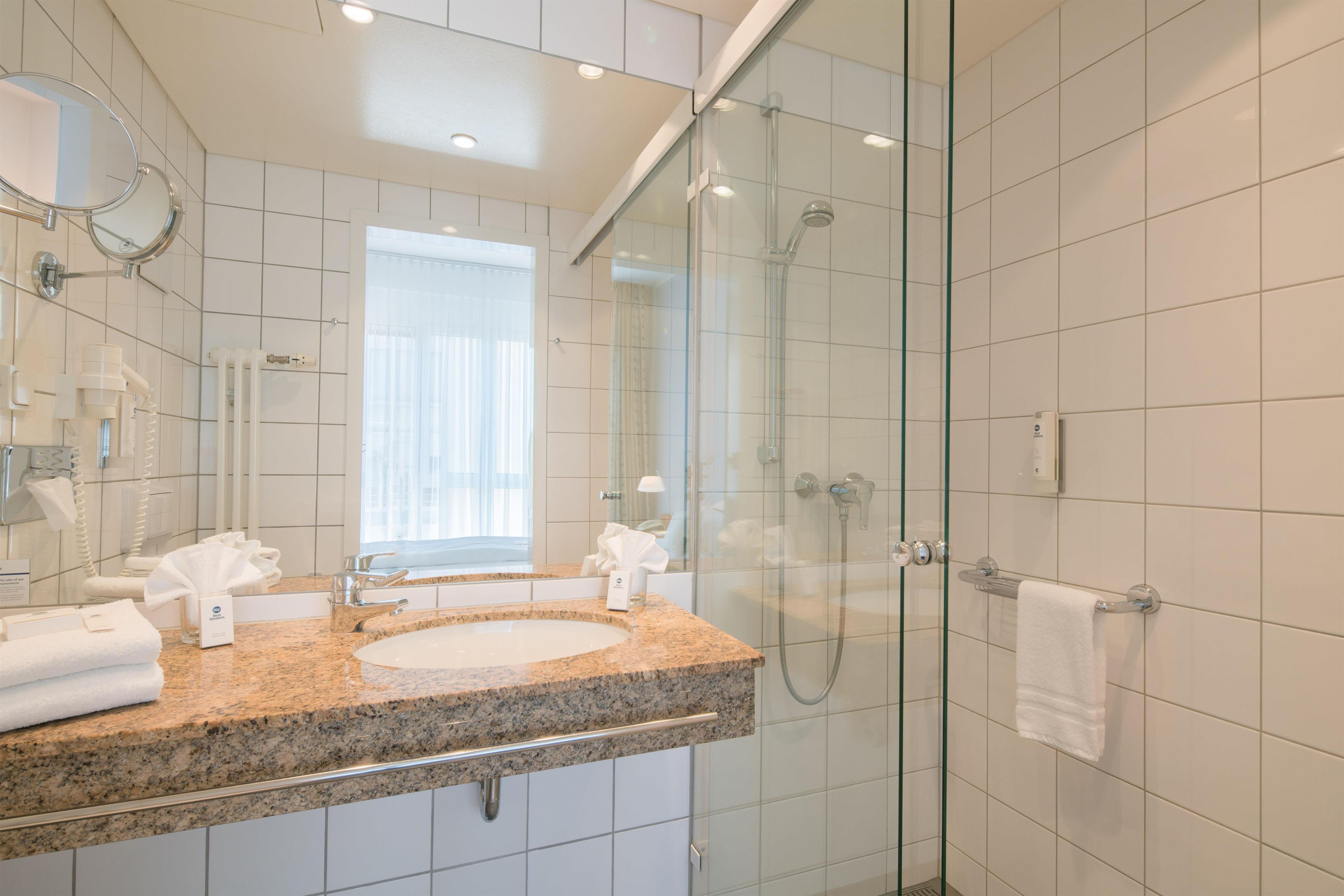 Une salle de bain moderne avec un comptoir en granit, deux vasques, une douche en verre et un grand miroir.