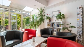 Un espace détente moderne avec des canapés en cuir rouge et noir, une table basse blanche et une bibliothèque remplie de livres et d’objets décoratifs.
