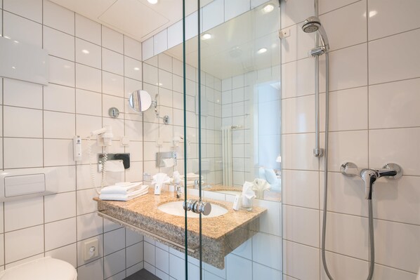 Un baño moderno con cabina de ducha de vidrio, lavamanos de encimera de granito y un espejo grande.