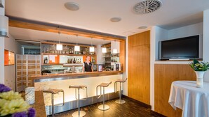 Zona de bar con un cantinero, taburetes, estanterías llenas de botellas y un televisor montado en la pared.