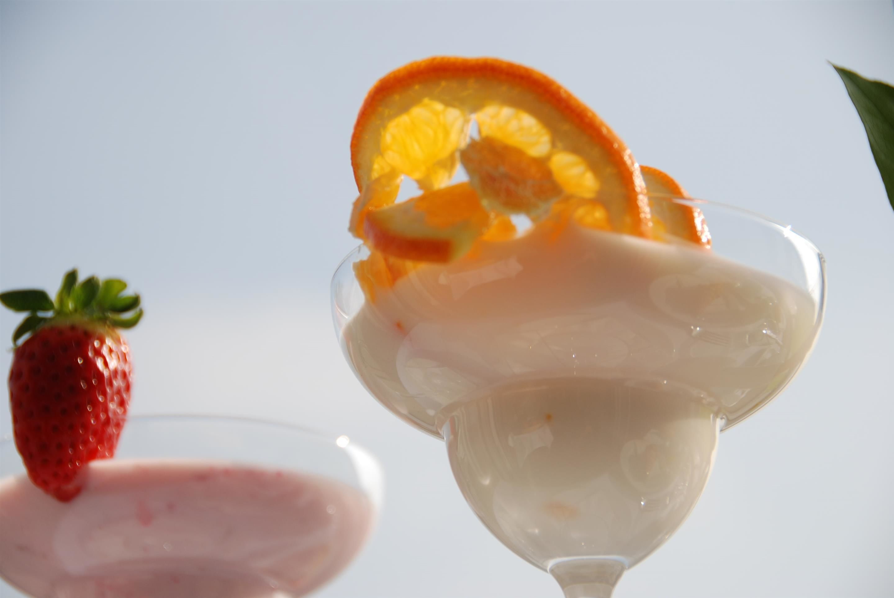 A glass with a creamy dessert topped with a strawberry and orange slice.