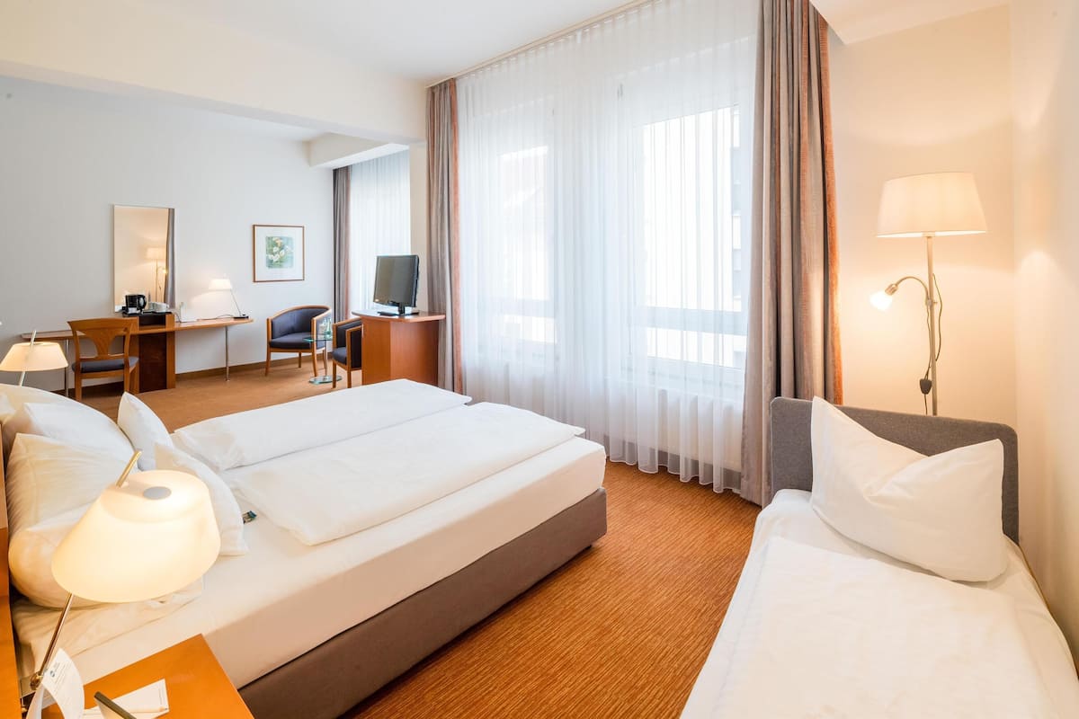 A hotel room with two beds, a desk, a chair, a TV, and a lamp.