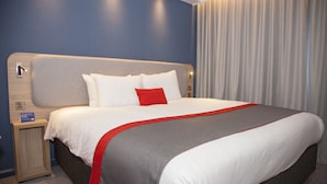 A hotel room with a large bed, a nightstand, and a wall-mounted lamp. - Holiday Inn Express Cardiff Bay by IHG (Cardiff)