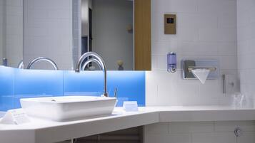 A modern bathroom with a white sink, a mirror, and a towel dispenser.