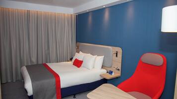Een hotelkamer met een bed, een rode stoel, een klein tafeltje en een nachtkastje.