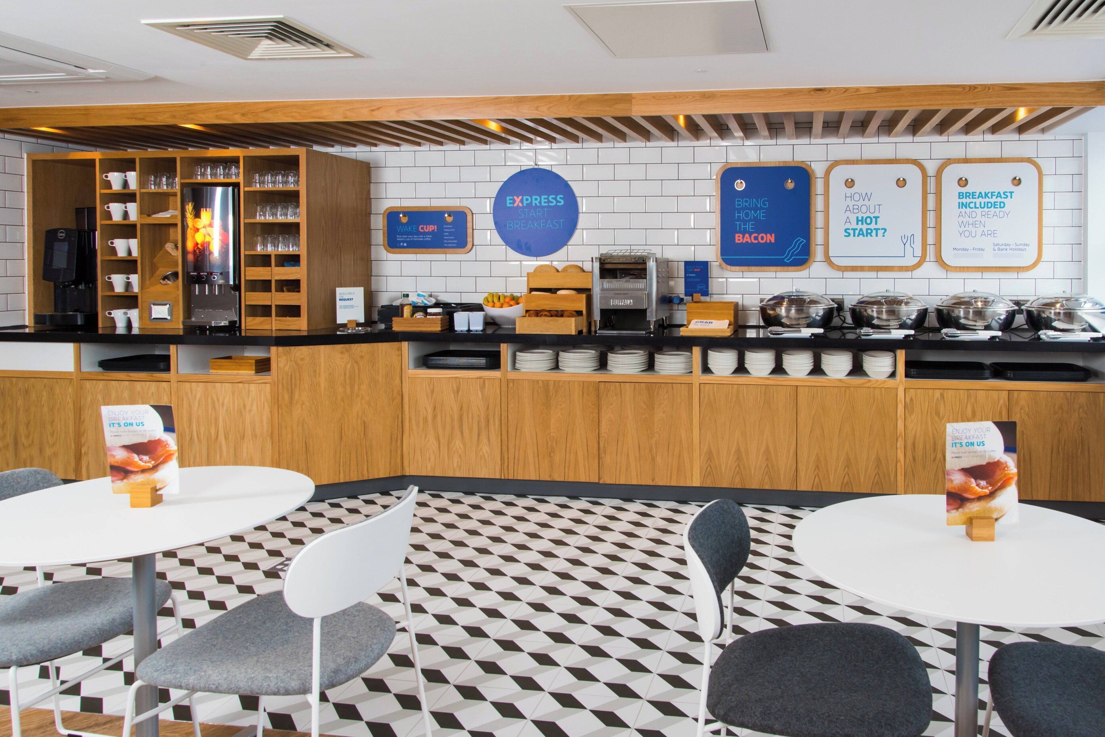 A breakfast area with a coffee machine, breakfast sign, and seating.