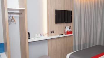 Une chambre d’hôtel avec un lit, un téléviseur fixé au mur, une petite table avec une bouilloire et des tasses, et un rideau.