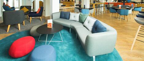Et moderne loungeområde med en buet sofa, runde puf og en bar i baggrunden.