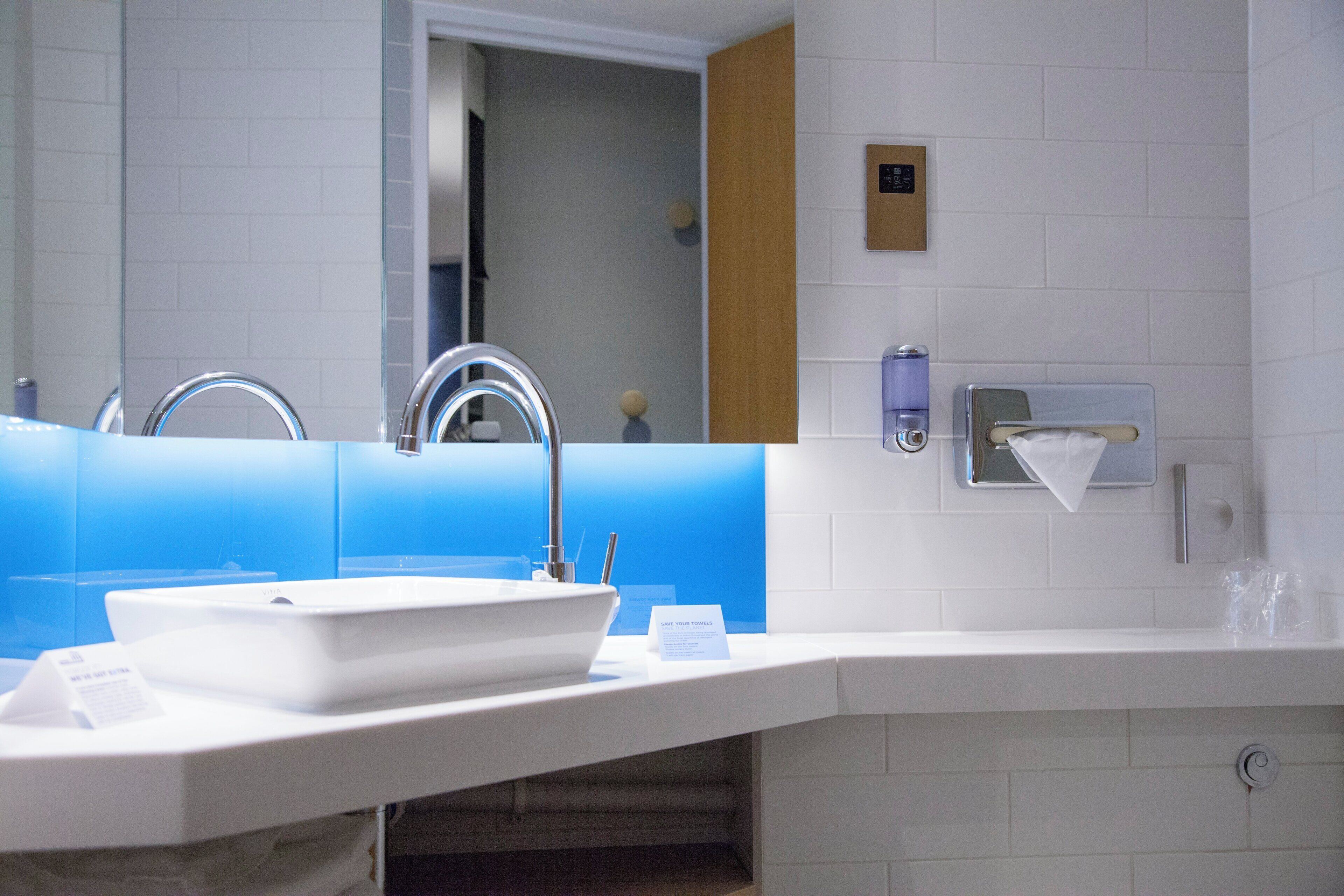 Une salle de bain moderne avec un lavabo blanc, un miroir et un mur d’accent bleu.