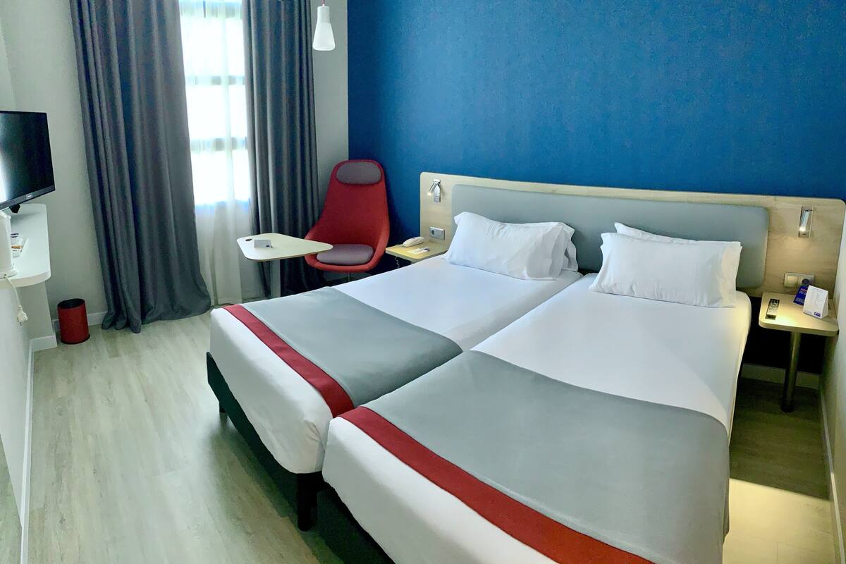 Habitación de hotel con dos camas, un televisor, una silla y un escritorio.
