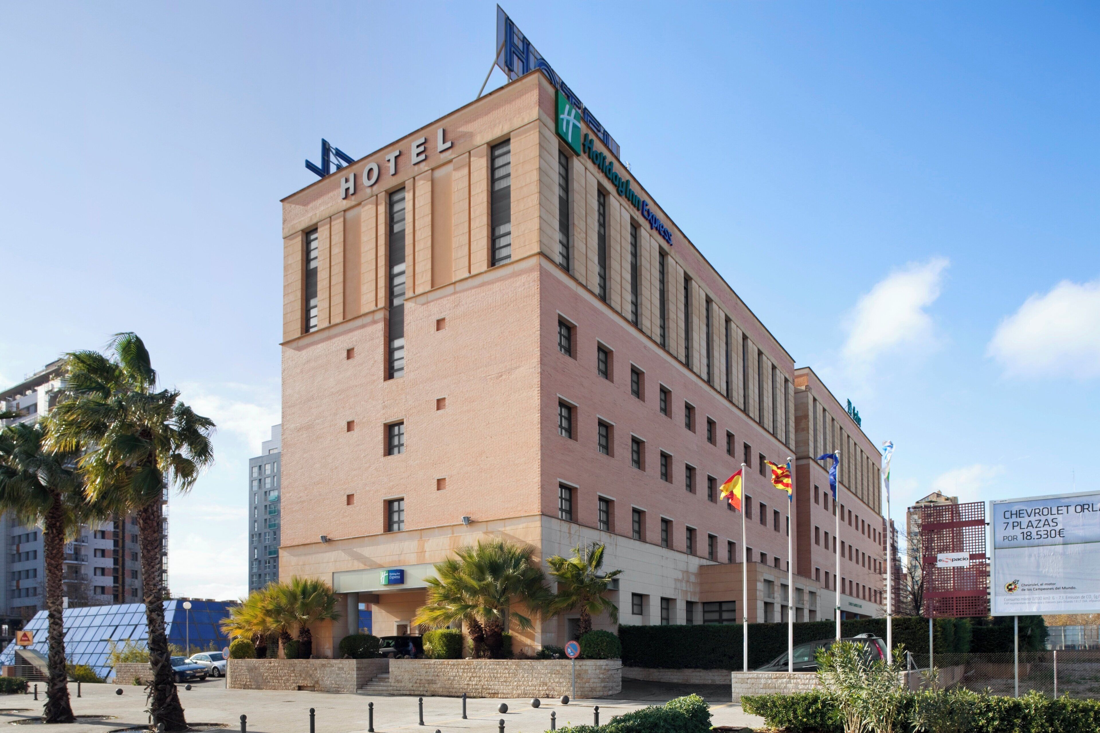 A multi-story hotel with a prominent 'HOTEL' sign on the facade, a 'Holiday Inn Express' logo, and several flags.