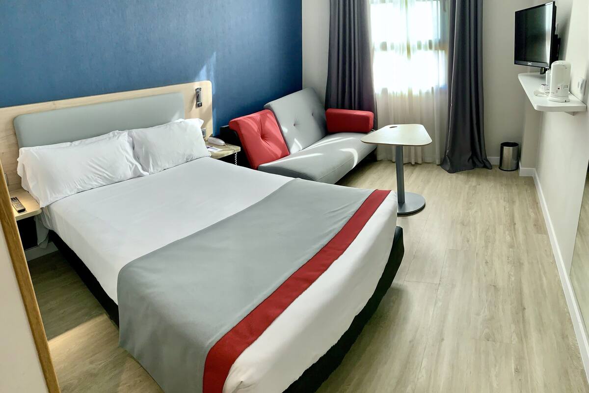 Habitación de hotel con una cama grande, un sofá, un televisor y una mesita de noche.