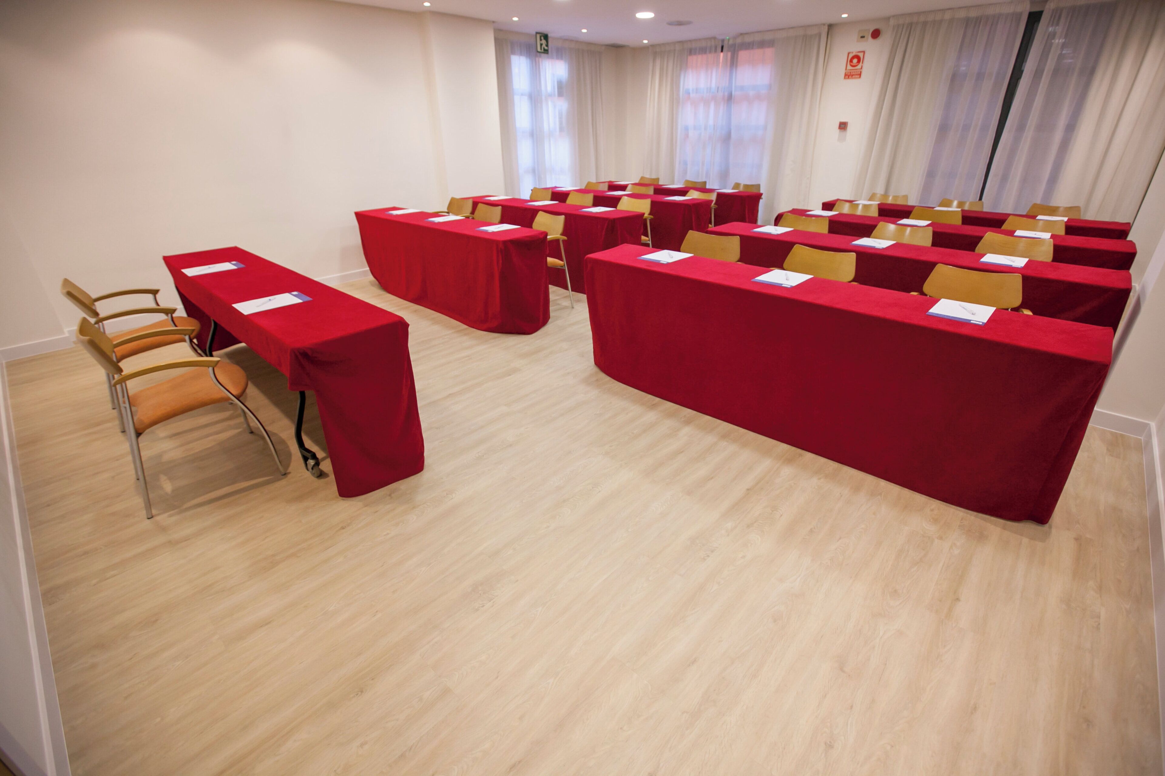 Ein Konferenzraum mit mehreren Tischen und Stühlen, einem Holzboden und einer weißen Wand mit Rauchmelder.