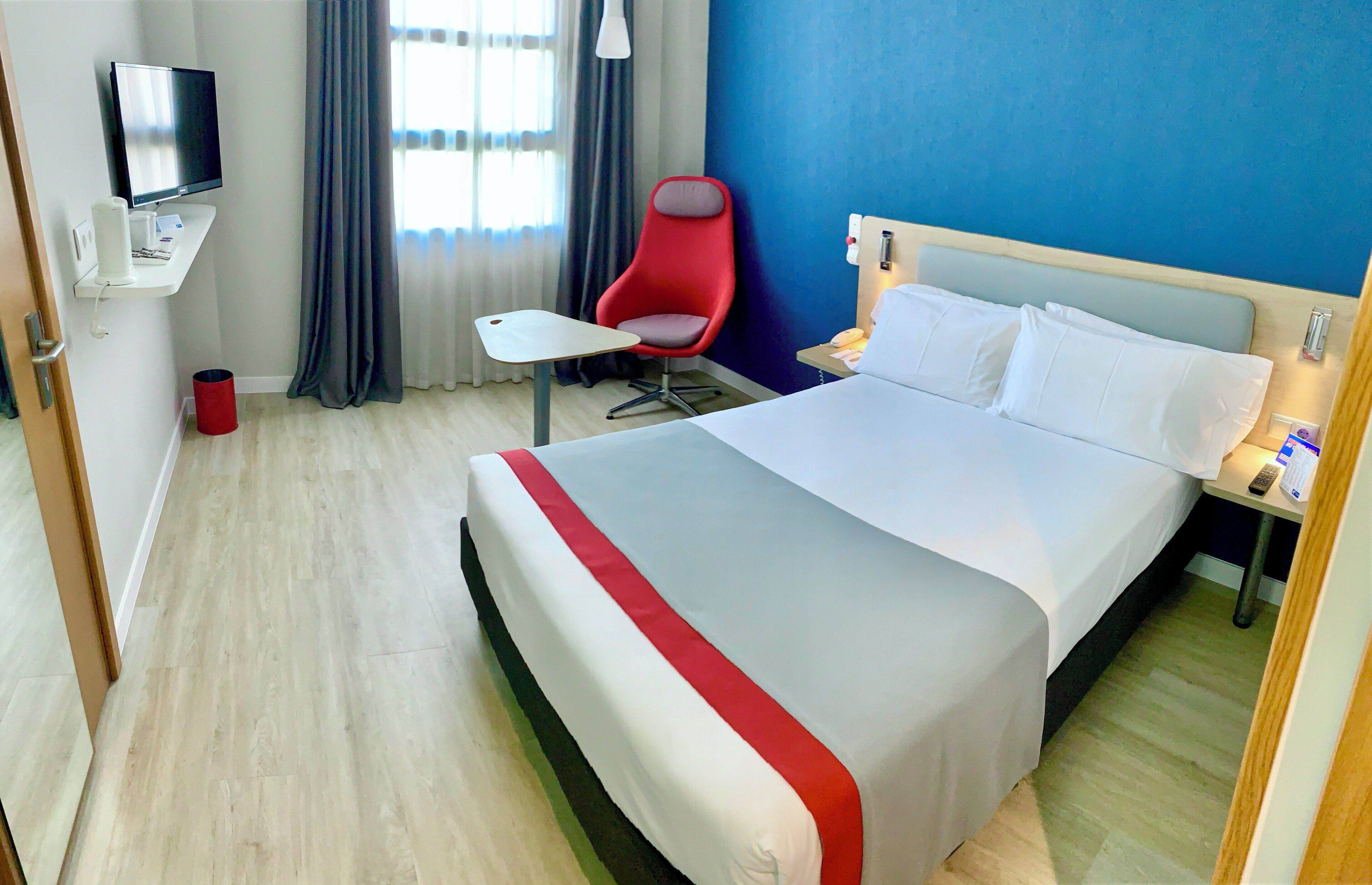 A hotel room with a bed, a desk, a chair, a TV, and a bathroom.