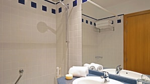 Een badkamer met een douche, een wastafel, een spiegel en een handdoekhouder.