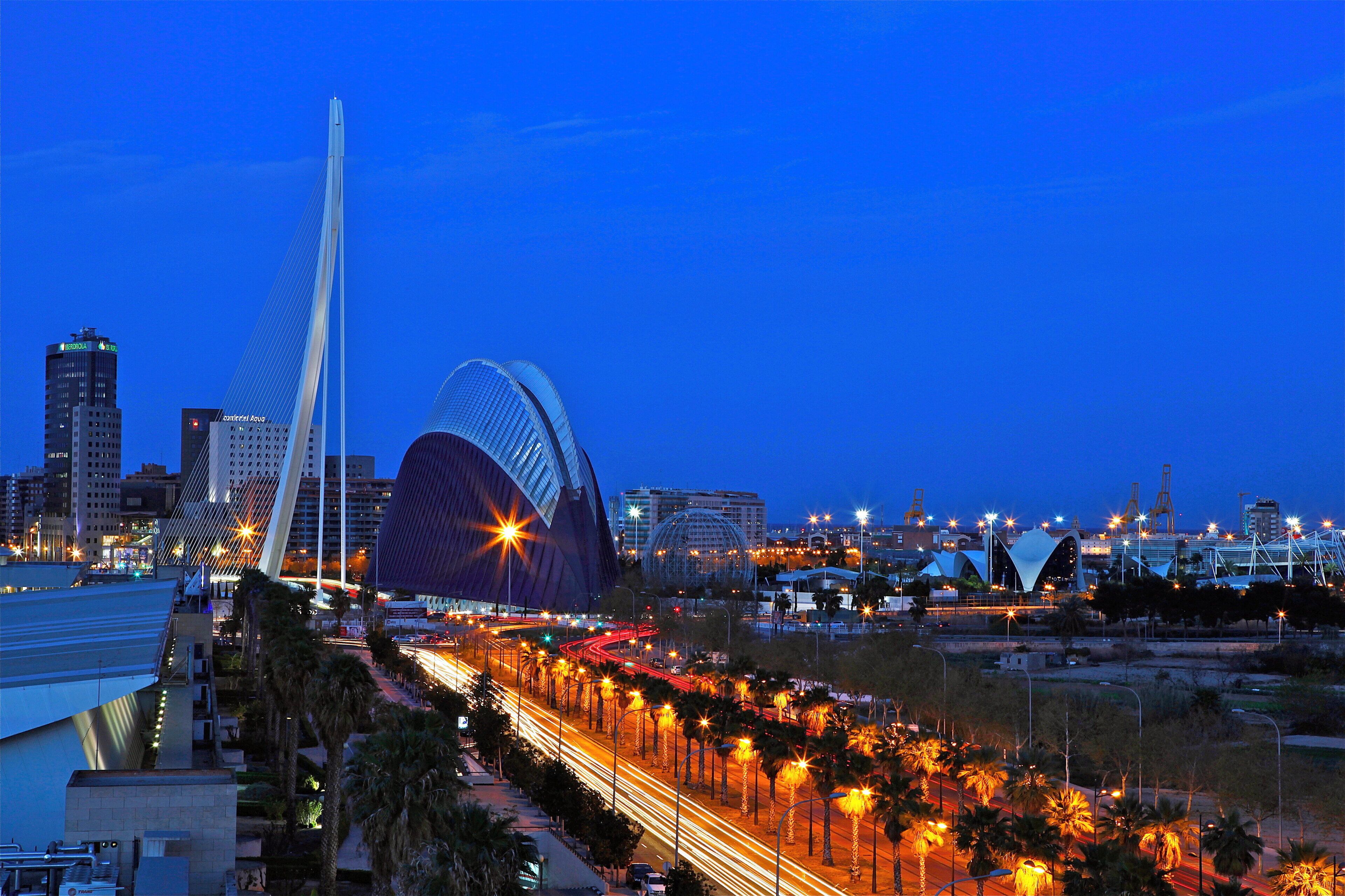 A cityscape at dusk with a prominent bridge and a distinctive building with a curved roof.