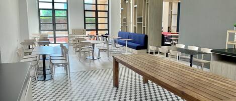 Een moderne binnenruimte met verschillende zithoeken, waaronder tafels en stoelen, en een lange bank.