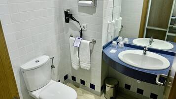 A bathroom with a toilet, two sinks, a mirror, and a trash can.