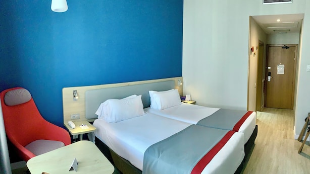 Een hotelkamer met een bed, een rode stoel, een klein tafeltje en een nachtkastje.