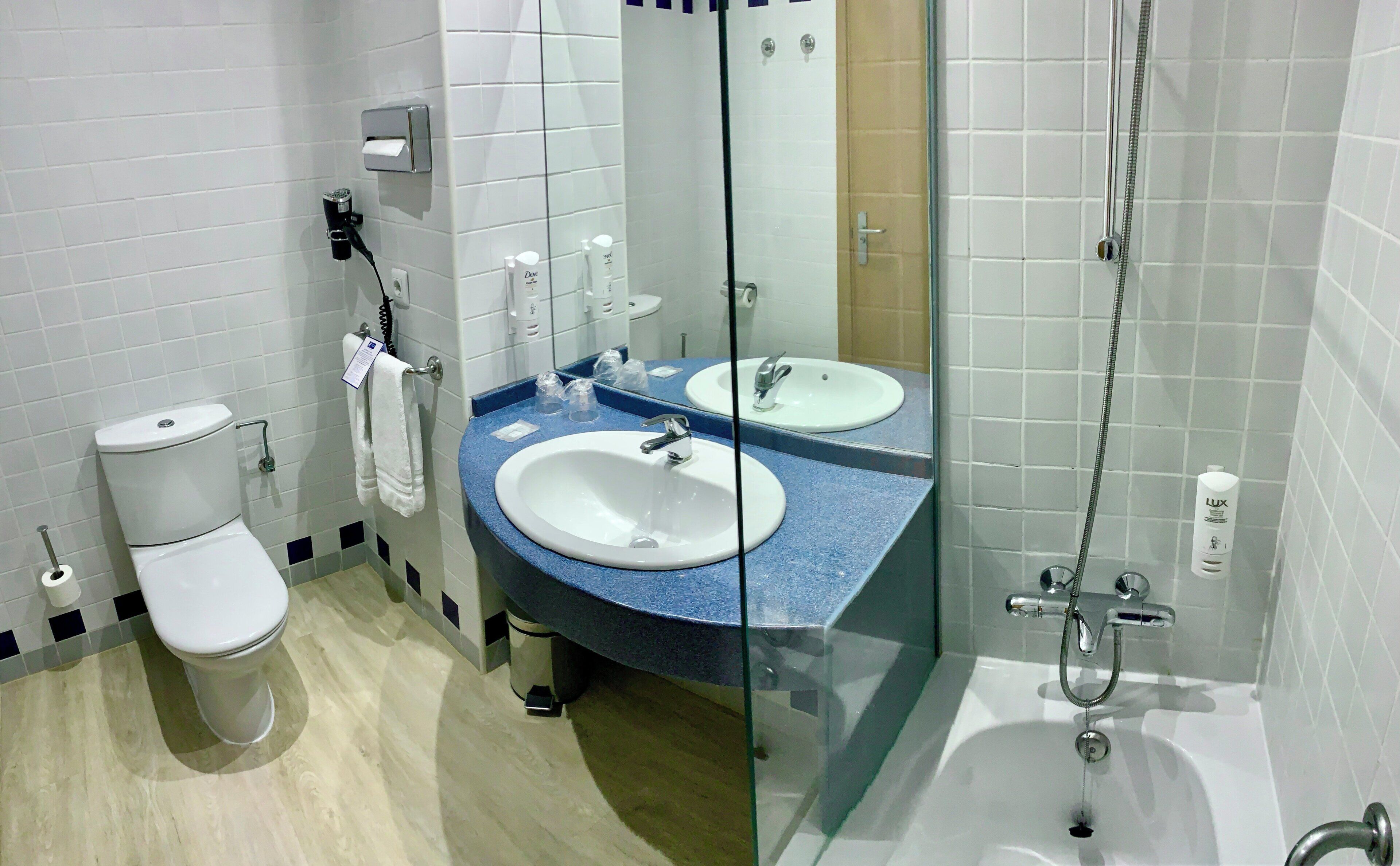Un baño con inodoro, dos lavamanos, cabina de ducha de vidrio y un espejo.