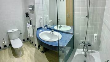 Un baño con inodoro, dos lavamanos, cabina de ducha de vidrio y un espejo.