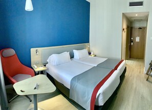 Une chambre d’hôtel avec un lit, un bureau, une chaise et une table de chevet.