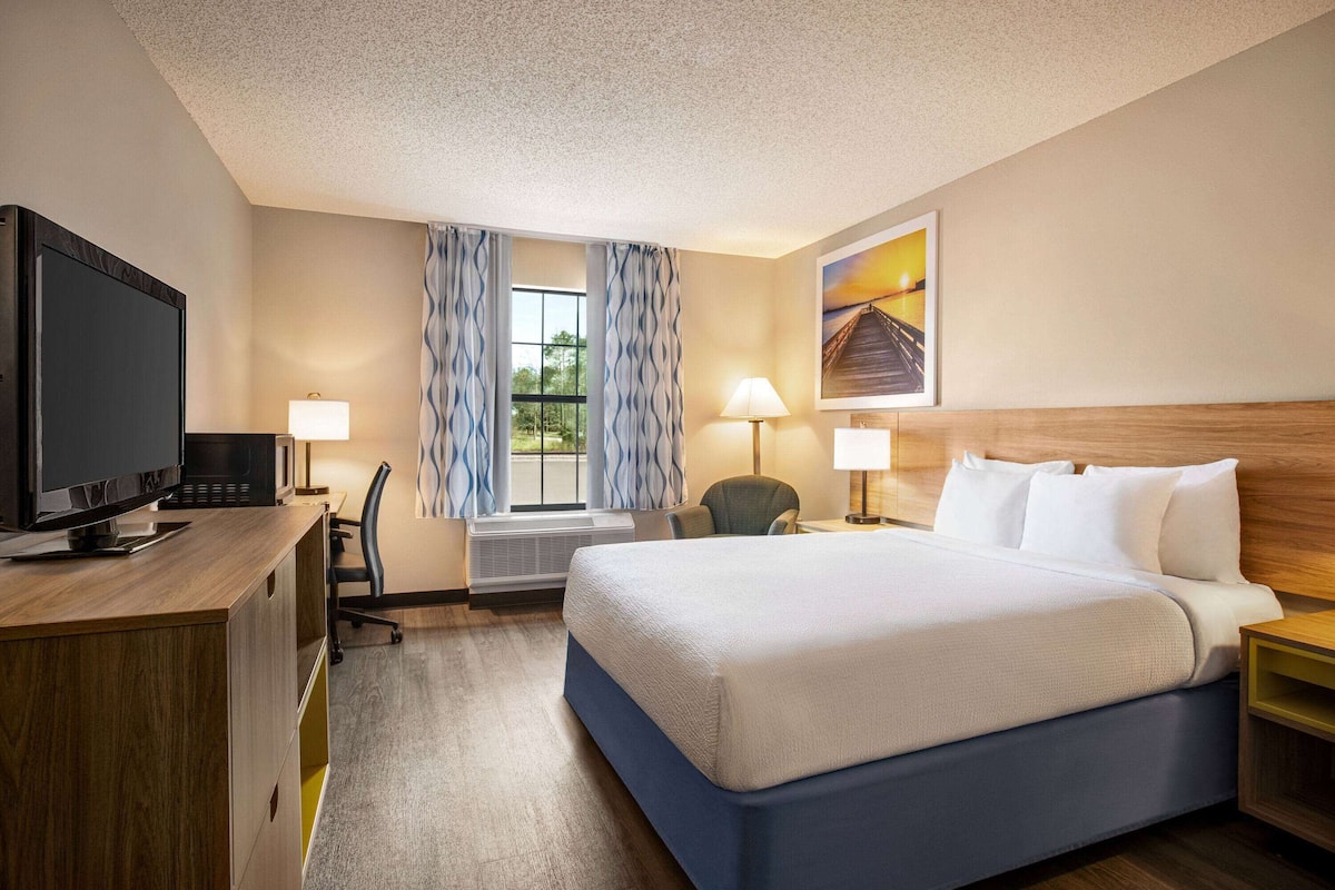 A hotel room with a bed, desk, TV, and two lamps.