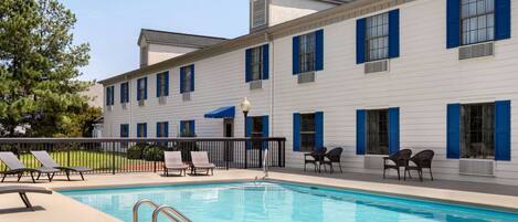 A pool area with lounge chairs and a building with blue shutters.