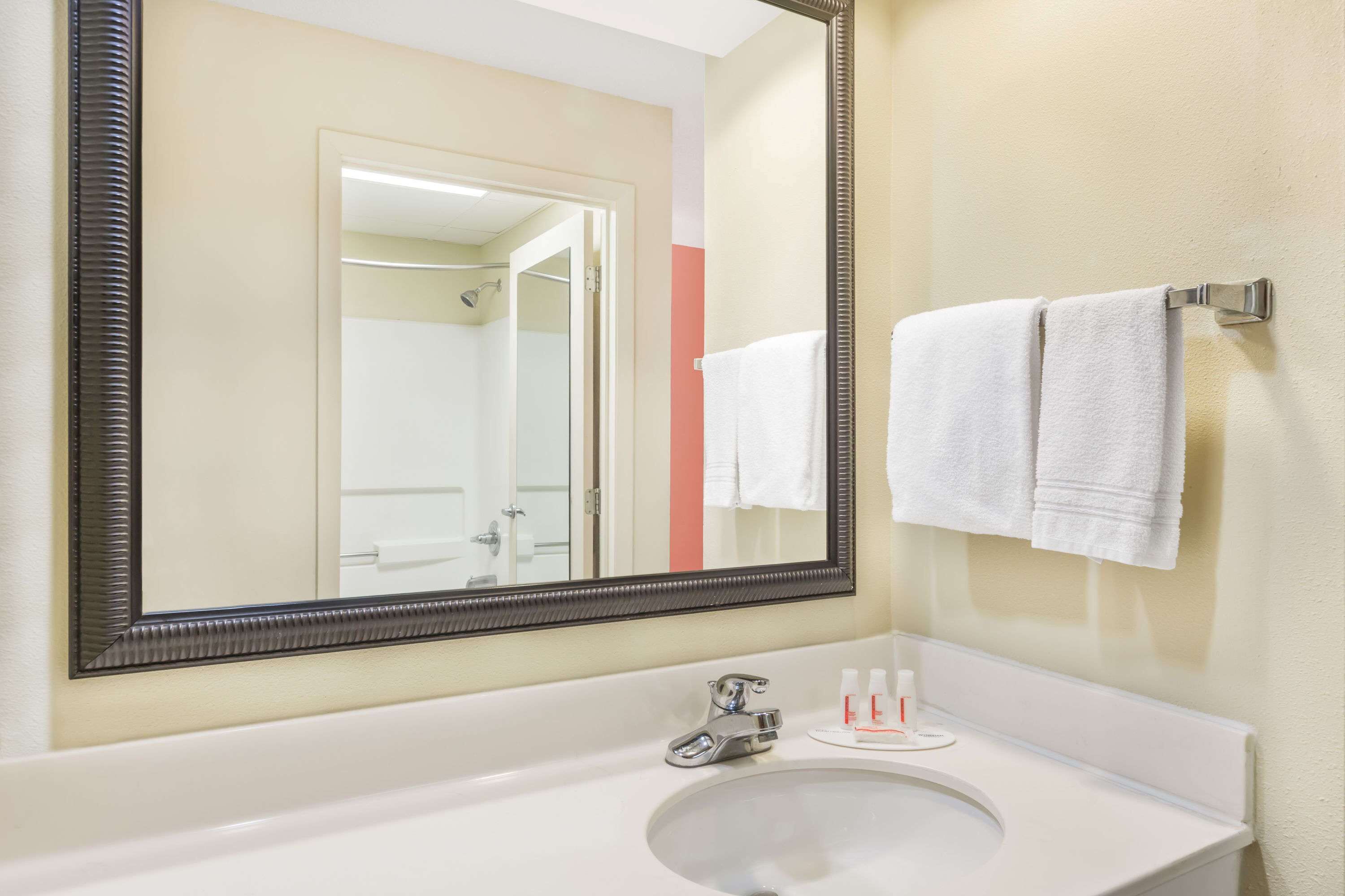Un baño con un espejo grande, un lavabo y dos toallas colgadas en un perchero.