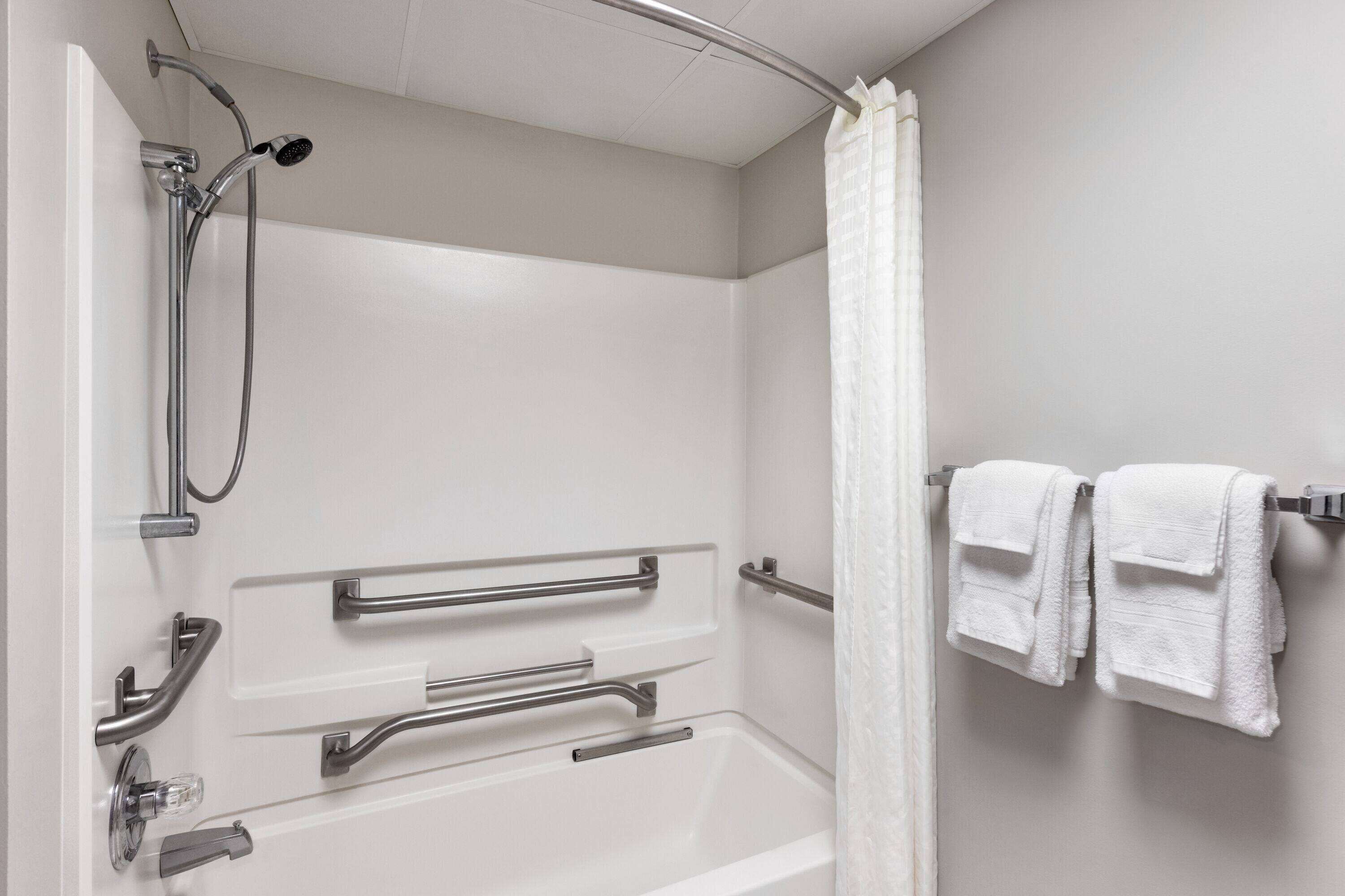 Een badkamer met een douche, handgrepen en een handdoekhouder.