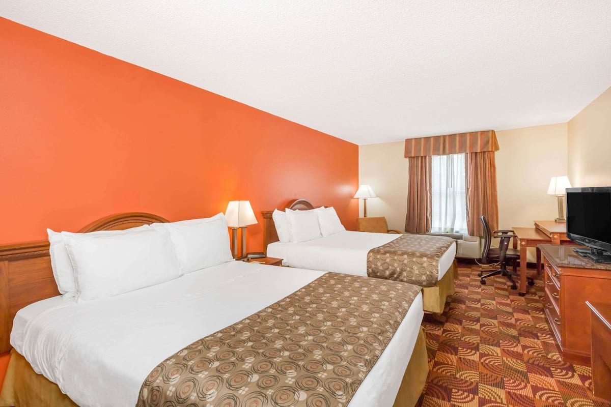A hotel room with two beds, a desk, a television, and a window with curtains.