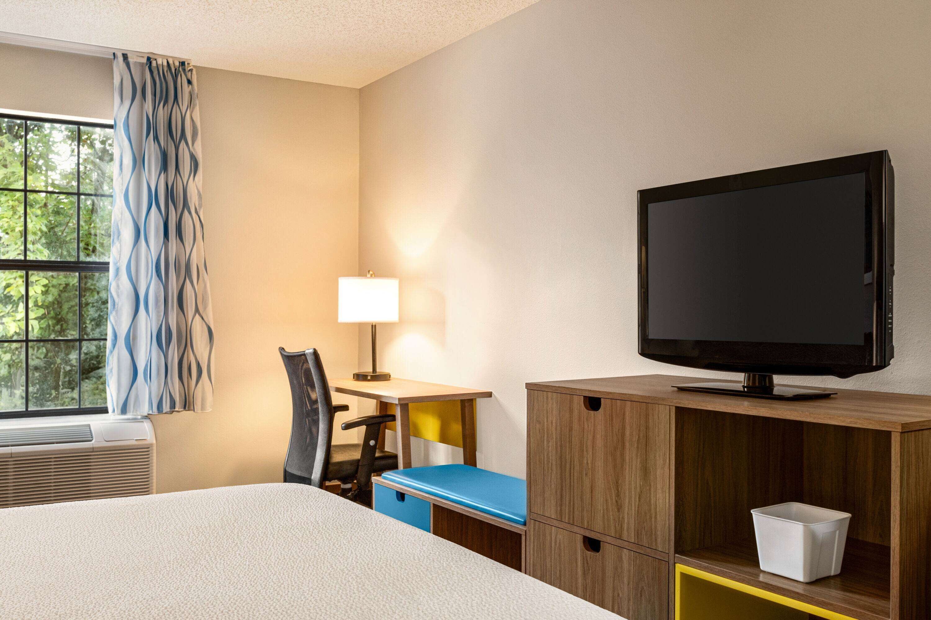 Een hotelkamer met een bed, een bureau met stoel, een televisie en een raam met gordijnen.
