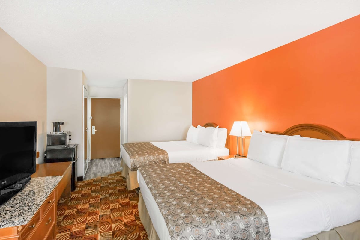 A hotel room with two beds, a TV, a desk, and a patterned carpet.