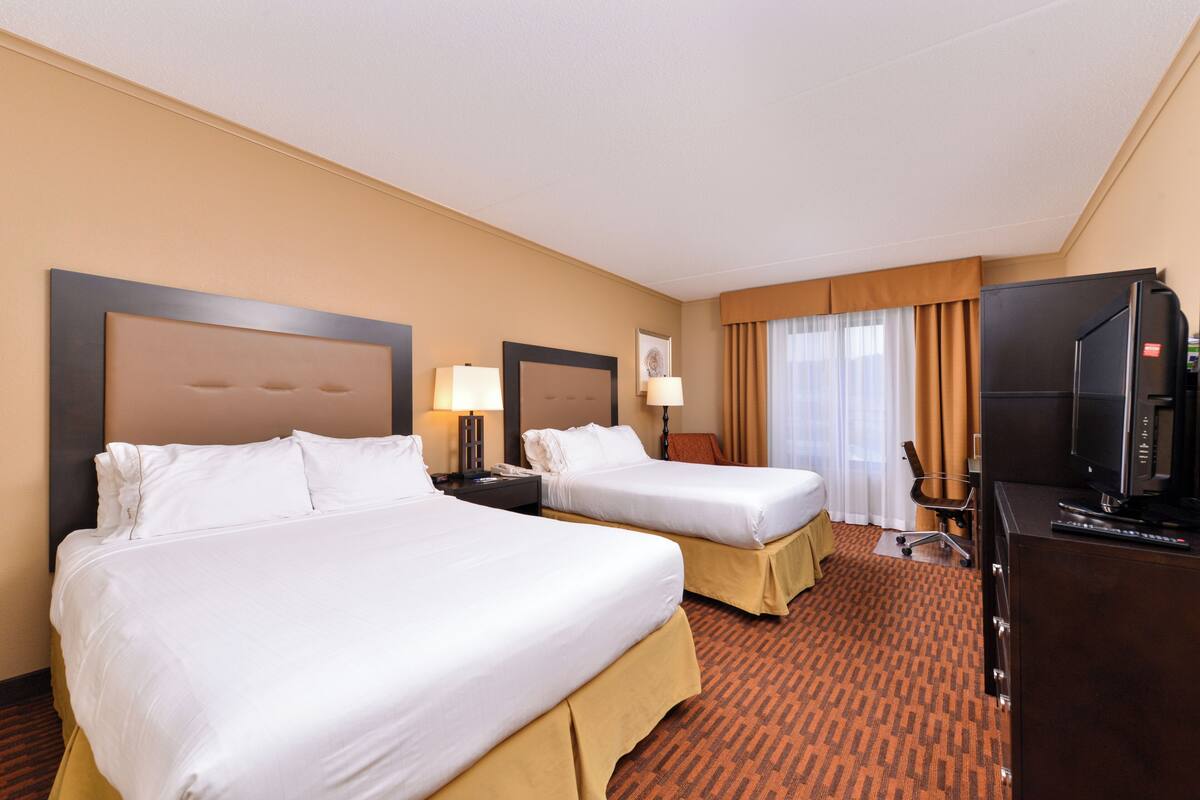 A hotel room with two beds, a desk with a television, and a window with curtains.