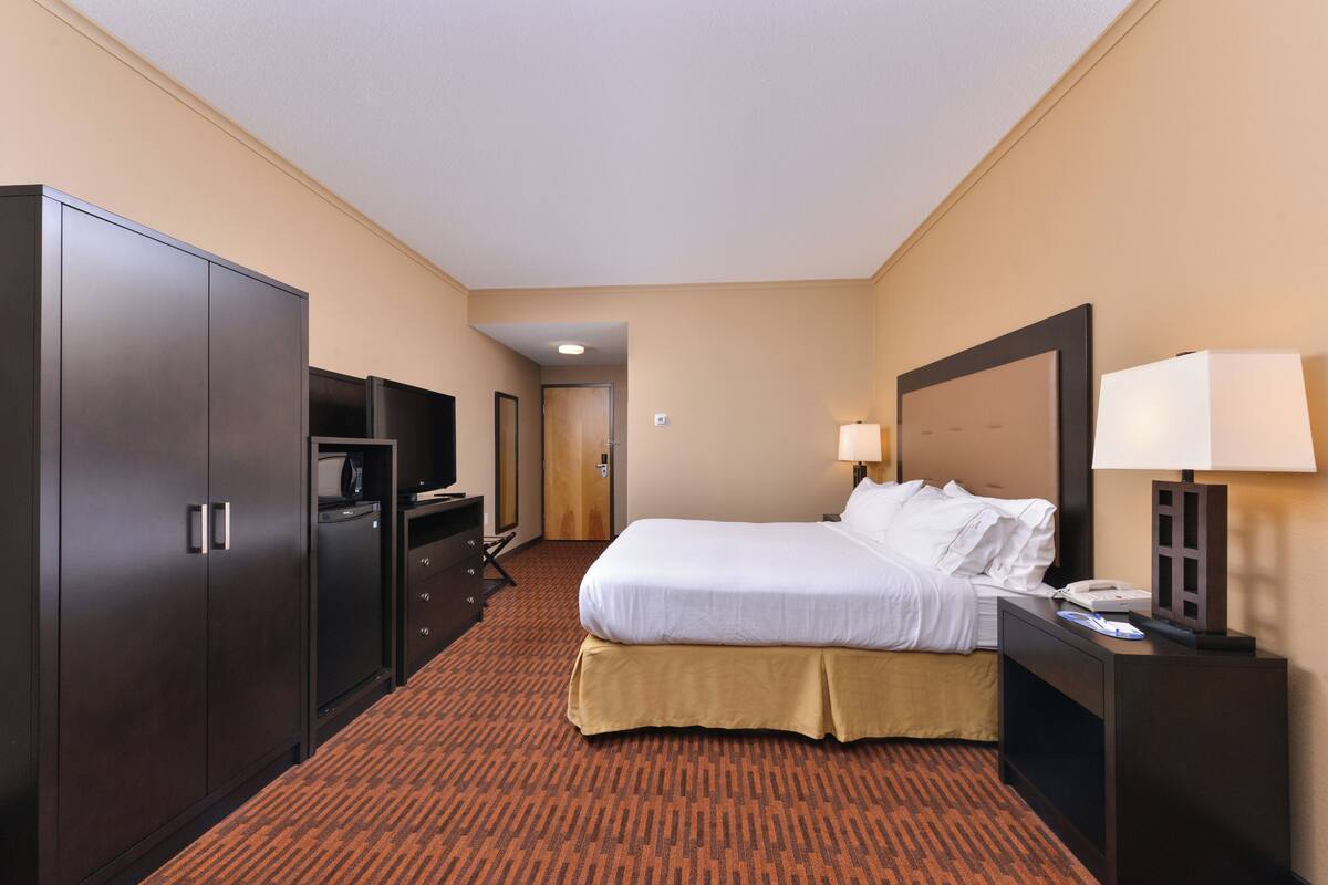 A hotel room with a large bed, a desk with a lamp, a wardrobe, and a television.