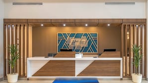 A reception desk with a modern design, a blue carpet, and two potted plants. - Holiday Inn Express Breezewood by IHG (Breezewood)