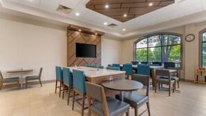 A modern dining area with multiple tables and chairs, a flat-screen TV mounted on a wooden wall, and large windows providing natural light. - Holiday Inn Express Breezewood by IHG (Breezewood)